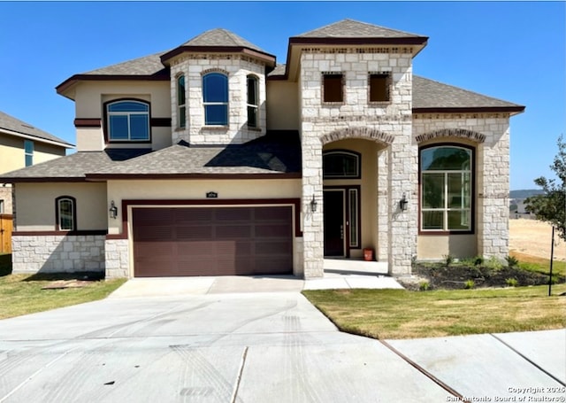 french country inspired facade featuring a garage, concrete driveway, roof with shingles, and stucco siding