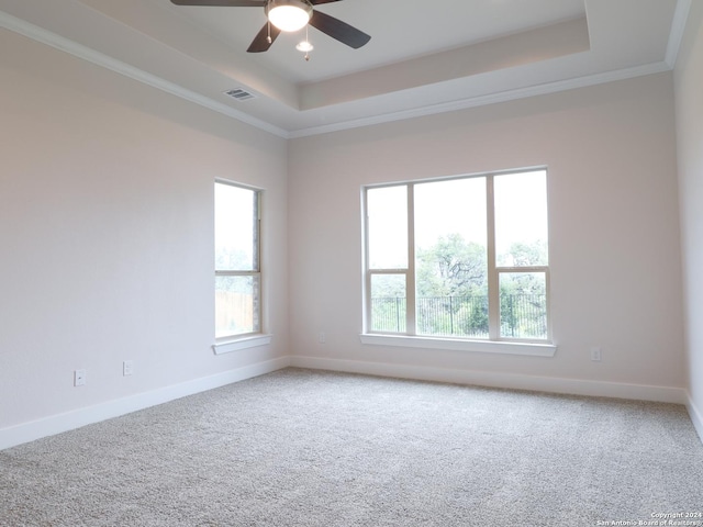 carpeted spare room featuring visible vents, baseboards, a raised ceiling, a ceiling fan, and ornamental molding