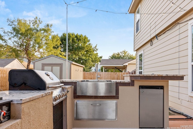 view of patio with an outbuilding, a sink, fence, grilling area, and a storage unit