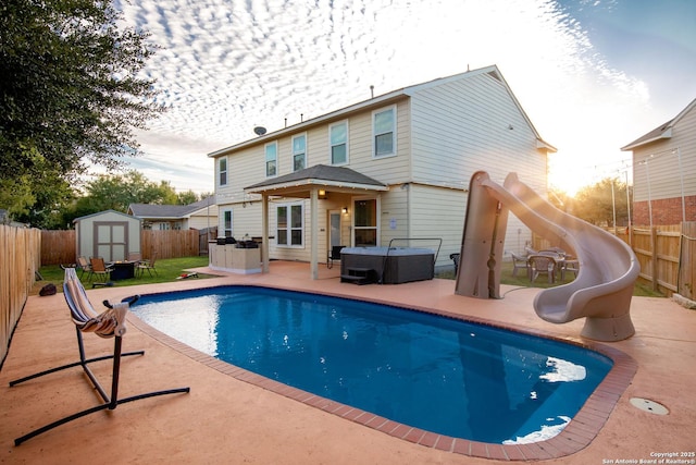 back of property with an outbuilding, a fenced backyard, a hot tub, and a storage shed