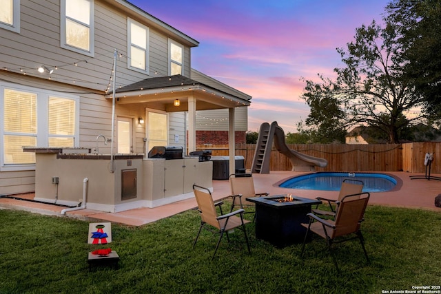 exterior space featuring a water slide, an outdoor fire pit, a fenced backyard, exterior kitchen, and a fenced in pool