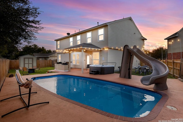 view of swimming pool with a fenced backyard, an outbuilding, a water slide, and a shed