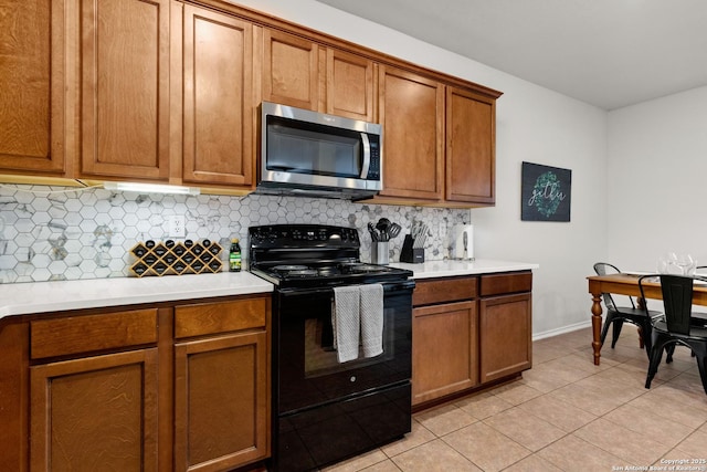 kitchen featuring black electric range, stainless steel microwave, light countertops, and brown cabinets