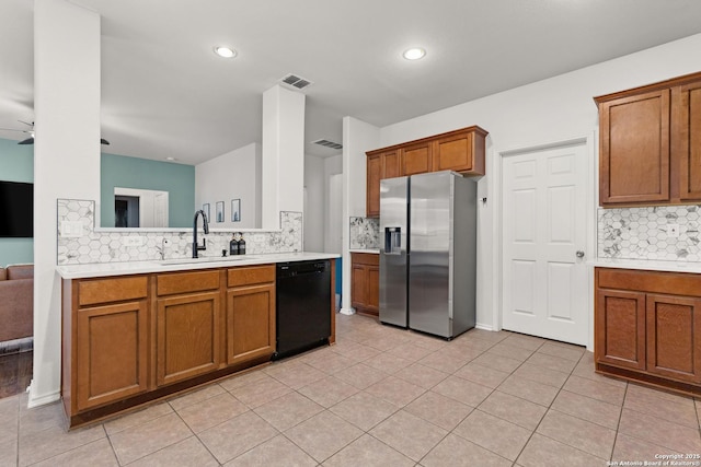 kitchen featuring a sink, light countertops, brown cabinets, dishwasher, and stainless steel fridge