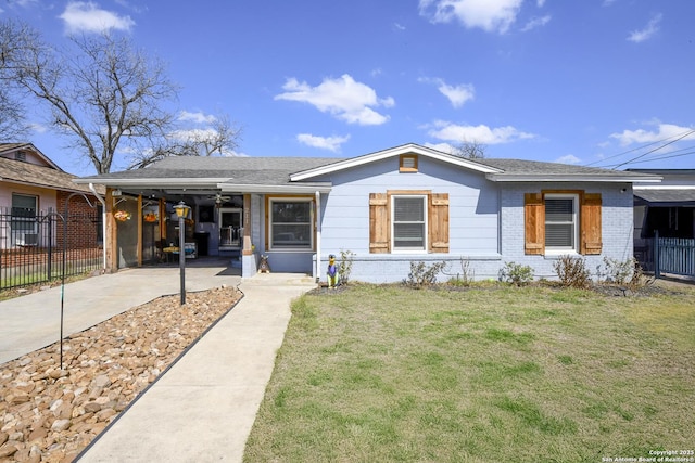 view of front of home with brick siding, fence, driveway, roof with shingles, and a front yard