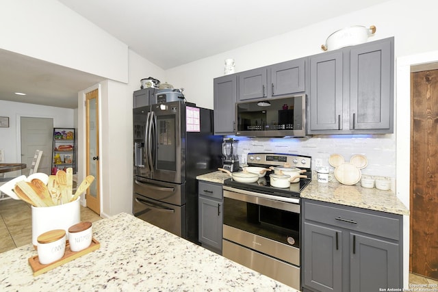 kitchen with tasteful backsplash, appliances with stainless steel finishes, gray cabinets, and light stone countertops