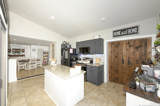 kitchen with light stone counters, a center island, stainless steel appliances, gray cabinets, and vaulted ceiling