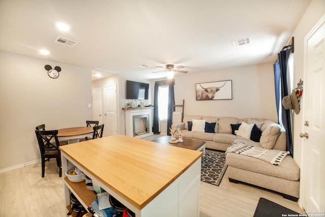 living room with ceiling fan, light wood-style flooring, a fireplace, and visible vents