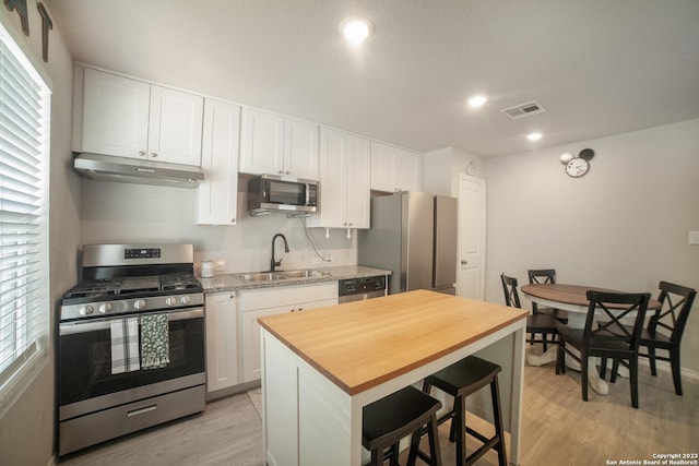 kitchen with butcher block counters, appliances with stainless steel finishes, white cabinets, a sink, and under cabinet range hood