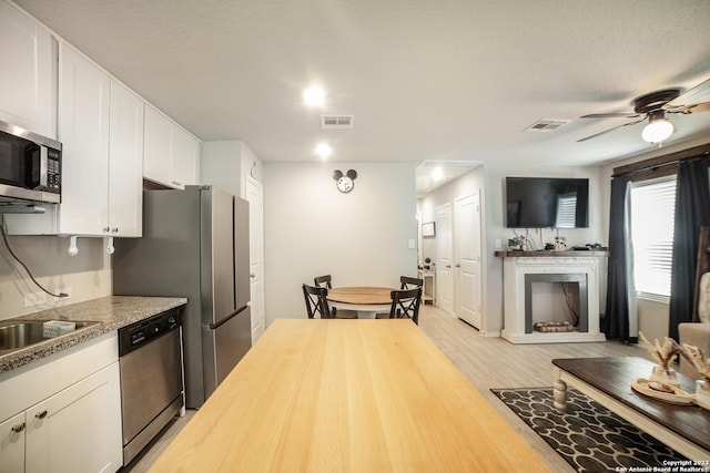 kitchen featuring a fireplace with raised hearth, appliances with stainless steel finishes, white cabinetry, butcher block countertops, and light wood-type flooring