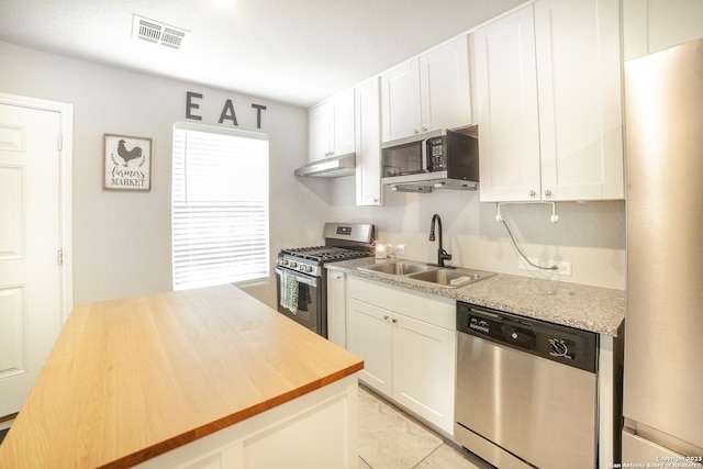 kitchen featuring visible vents, wooden counters, appliances with stainless steel finishes, a sink, and under cabinet range hood