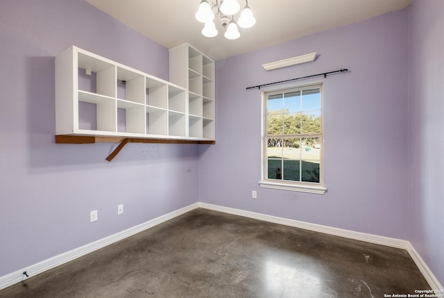 unfurnished room featuring concrete floors, an inviting chandelier, and baseboards