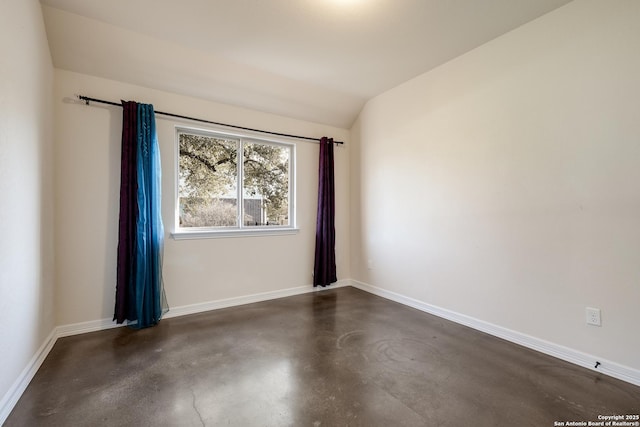 unfurnished room with lofted ceiling, concrete floors, and baseboards