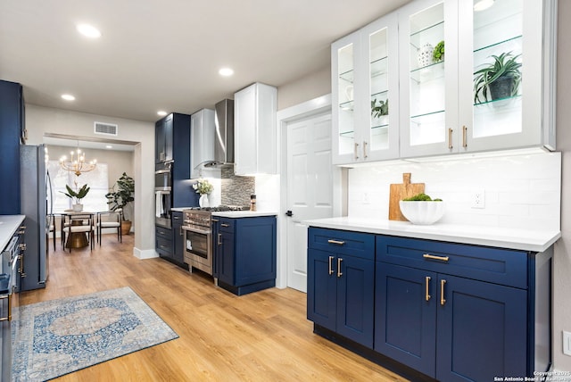 kitchen with blue cabinetry, stainless steel appliances, light countertops, white cabinets, and wall chimney exhaust hood