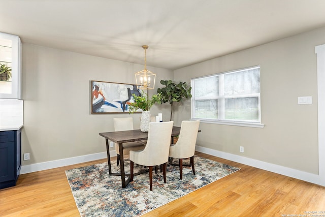 dining area with light wood-type flooring, baseboards, and a notable chandelier