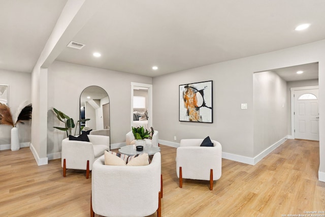 living area featuring arched walkways, visible vents, light wood finished floors, and recessed lighting