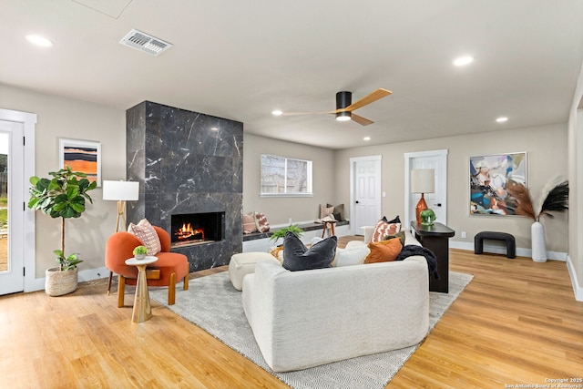 living room with recessed lighting, a premium fireplace, wood finished floors, visible vents, and baseboards