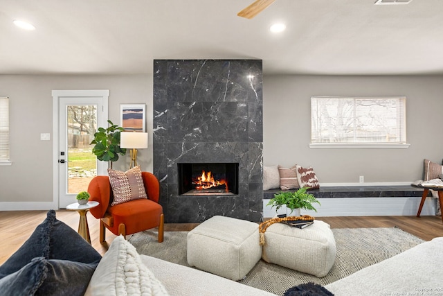 living area featuring recessed lighting, a premium fireplace, wood finished floors, visible vents, and baseboards