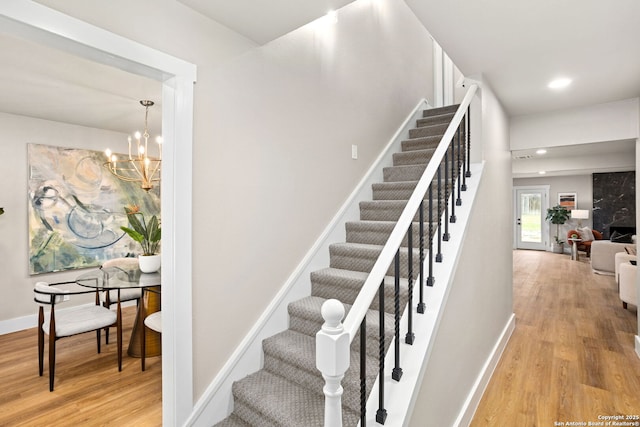 stairs featuring baseboards, a chandelier, wood finished floors, and recessed lighting