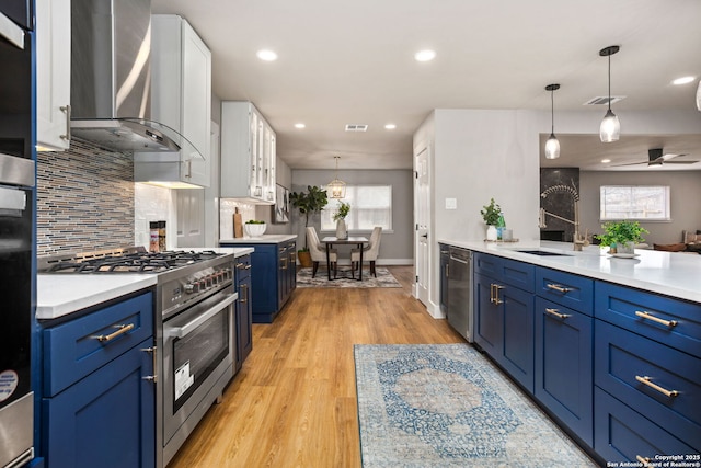 kitchen featuring stainless steel appliances, white cabinets, light countertops, wall chimney range hood, and blue cabinetry