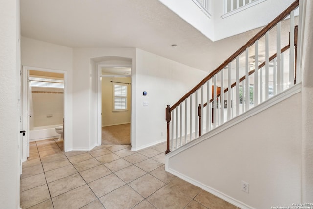 foyer entrance with arched walkways, stairway, baseboards, and tile patterned floors