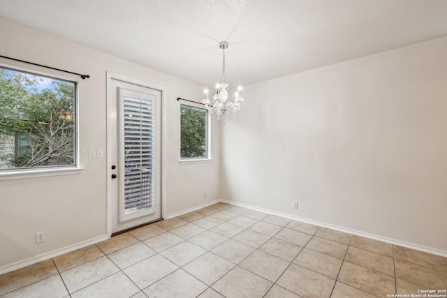 unfurnished dining area featuring a notable chandelier, baseboards, and light tile patterned floors