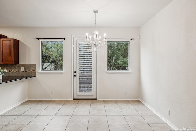 unfurnished dining area with an inviting chandelier, baseboards, and light tile patterned flooring