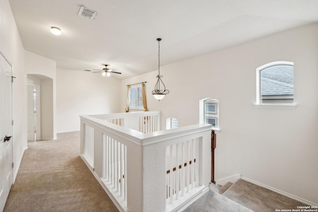 hallway featuring baseboards, visible vents, arched walkways, light colored carpet, and an upstairs landing