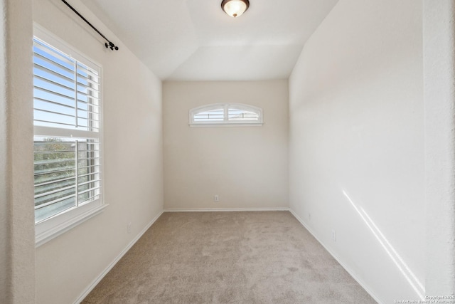 empty room featuring baseboards, vaulted ceiling, and light colored carpet