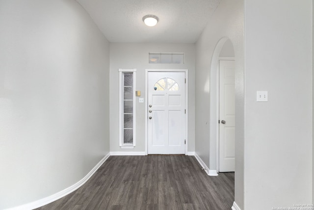 entryway featuring arched walkways, dark wood-style flooring, a textured ceiling, and baseboards