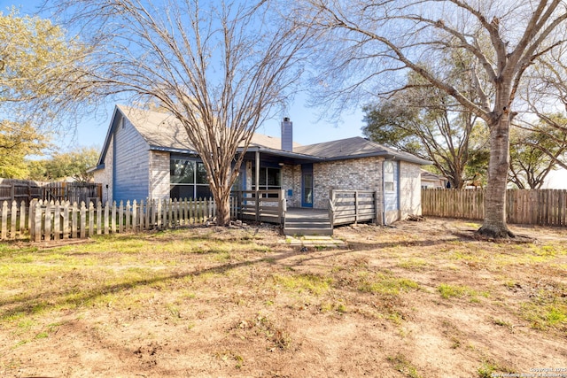 view of front of property with a deck, brick siding, a chimney, and a fenced backyard