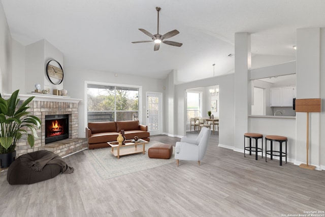 living room featuring ceiling fan with notable chandelier, a fireplace, wood finished floors, and baseboards