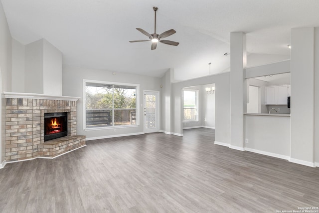 unfurnished living room featuring ceiling fan with notable chandelier, a fireplace, wood finished floors, and baseboards