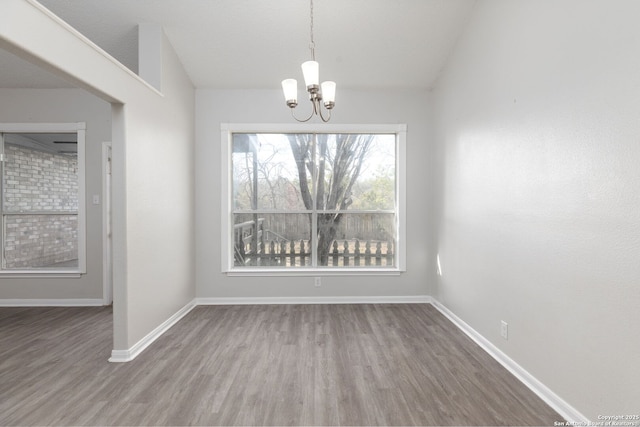 unfurnished dining area featuring an inviting chandelier, baseboards, vaulted ceiling, and wood finished floors