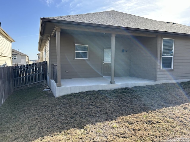 rear view of house with a yard, roof with shingles, fence, and a patio