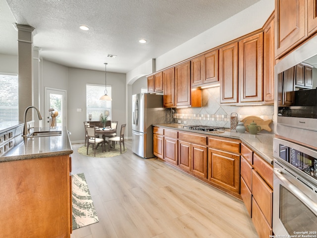 kitchen with stainless steel appliances, brown cabinets, a sink, and tasteful backsplash