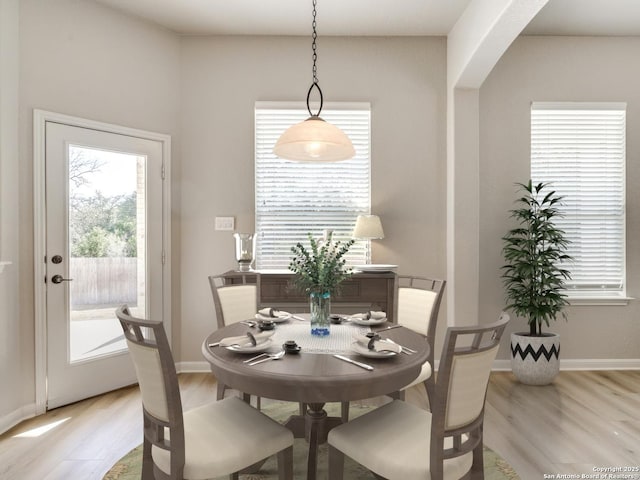 dining room featuring arched walkways, light wood-style flooring, and baseboards