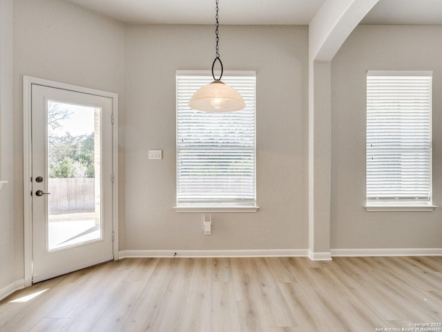 unfurnished dining area featuring arched walkways, baseboards, and light wood finished floors