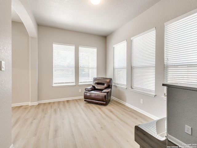 living area featuring a textured ceiling, baseboards, arched walkways, and wood finished floors