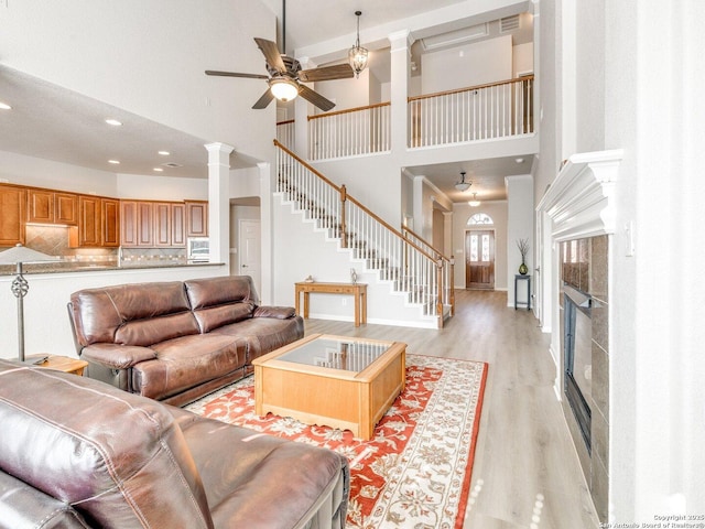 living room featuring visible vents, stairway, light wood finished floors, a glass covered fireplace, and ornate columns