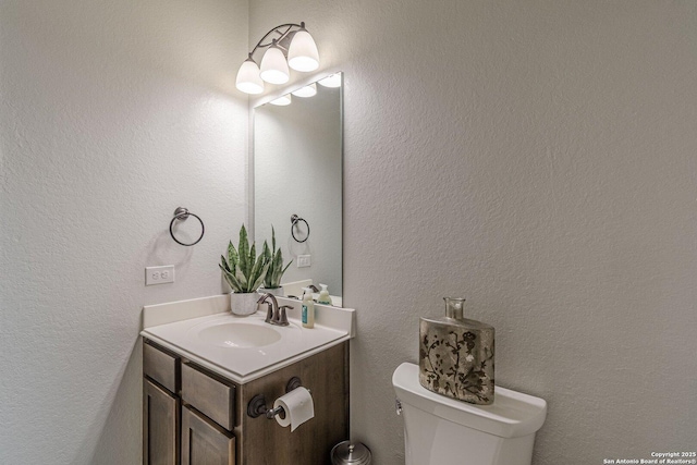 bathroom with toilet, a textured wall, and vanity