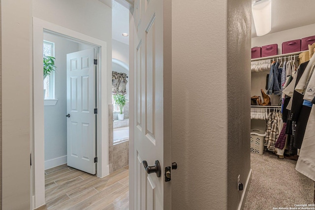 corridor with baseboards, a textured wall, and light wood finished floors