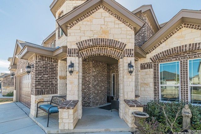 entrance to property with a garage, stone siding, brick siding, and driveway