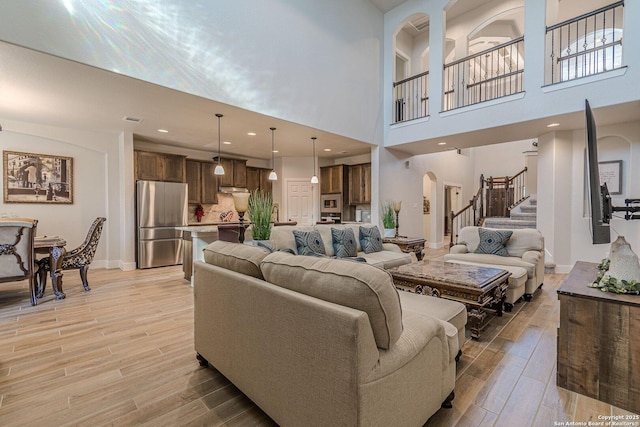 living area featuring stairway, light wood-type flooring, arched walkways, and baseboards