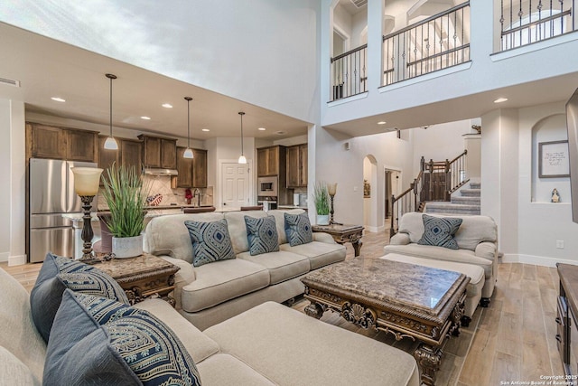 living room with baseboards, arched walkways, stairs, light wood-type flooring, and recessed lighting