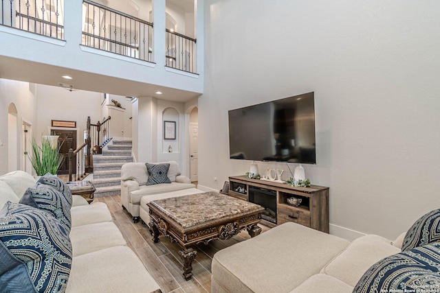 living area with arched walkways, light wood-type flooring, stairs, and baseboards