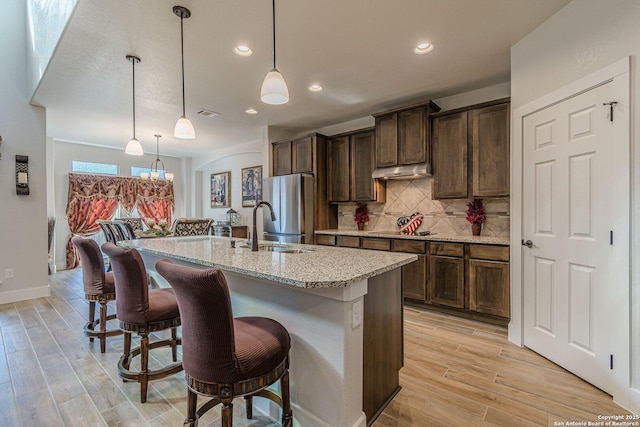 kitchen with light wood finished floors, a kitchen breakfast bar, backsplash, freestanding refrigerator, and a sink