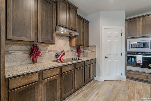 kitchen with under cabinet range hood, dark brown cabinets, appliances with stainless steel finishes, light wood-type flooring, and decorative backsplash