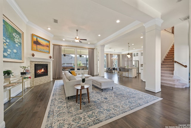 living area featuring dark wood-style floors, crown molding, stairway, a ceiling fan, and ornate columns