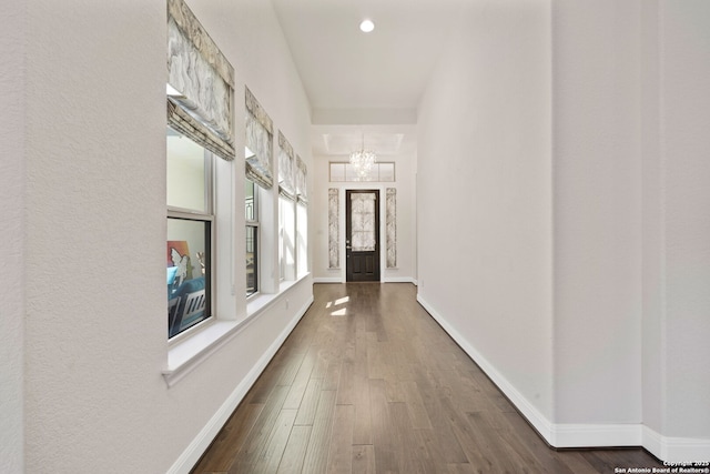 corridor featuring dark wood-style floors, recessed lighting, a notable chandelier, and baseboards